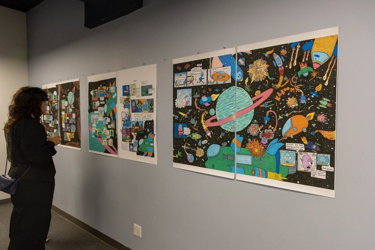 A gallery wall hung with rows of framed comic pages, a visitor standing at the far end