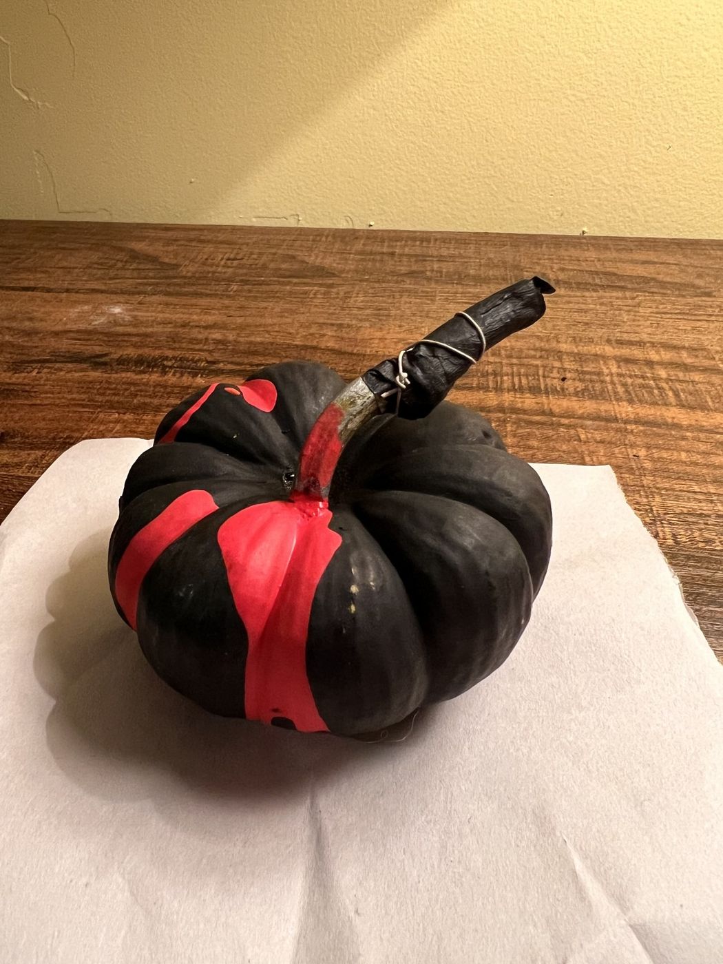 A pumpkin painted matte black with a red ribbon around it and a black painted stem